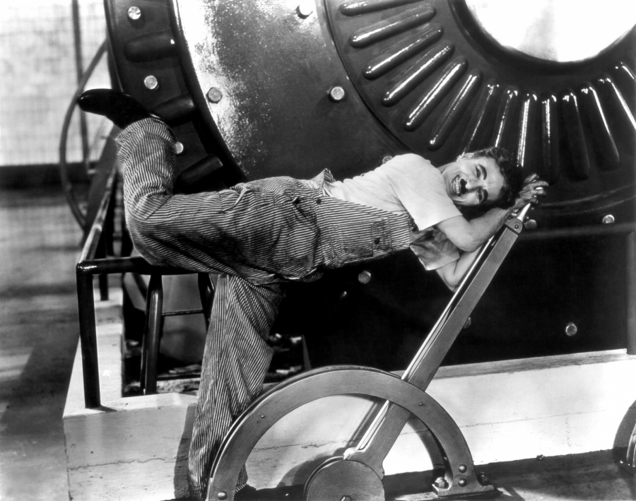 Posing for a photoshoot to advertise his film, Charlie Caplin leans over a lever. 