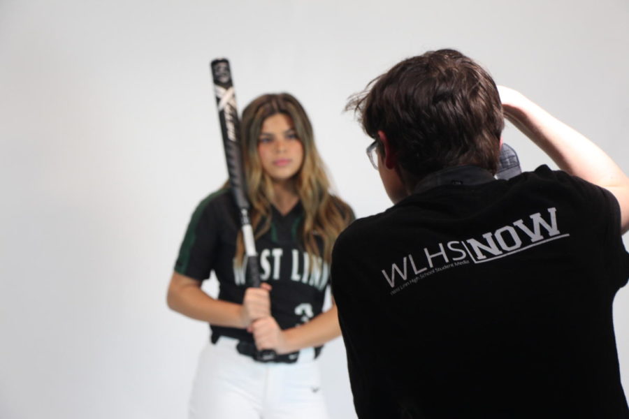 A photographer takes a  photo of a softball player for their player profile. 