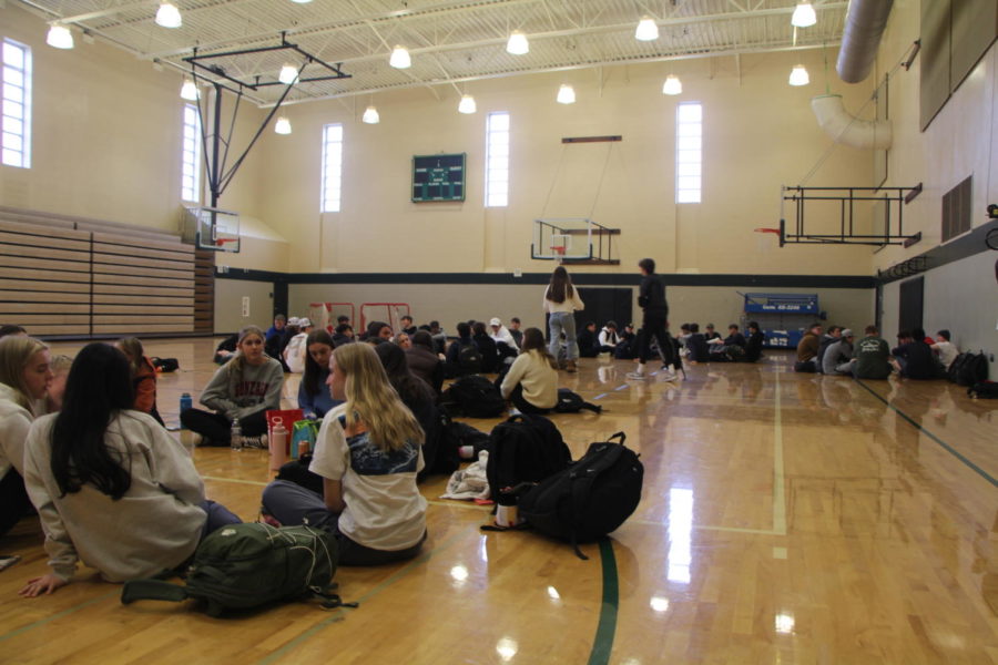 Students sit on the gym floor as they listen to 
the speaker of the day and discuss with their group of friends.	