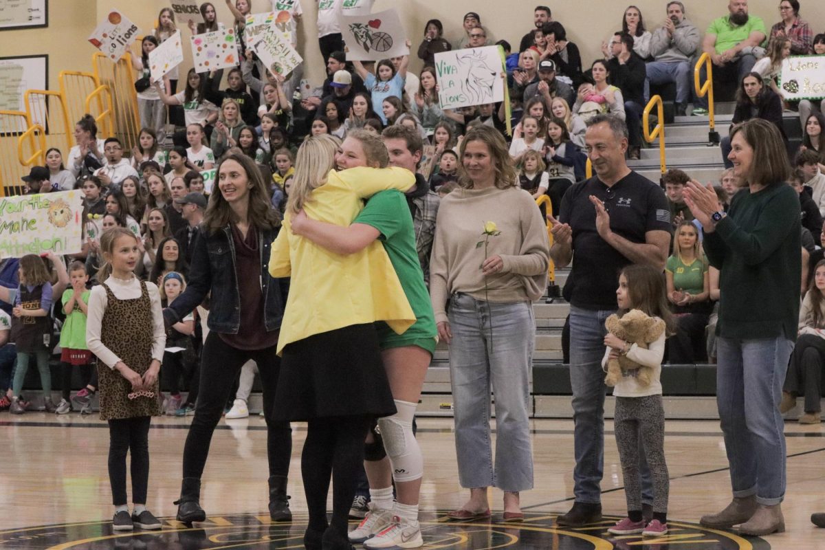Poppy Friel, senior, hugs head coach Brooke Gates during her recognition. Traditionally during senior nights, family joins the player as they’re acknowledged for their work on the team. Here, they are lined up in the center of the court, while audience members hold signs from a distance. 