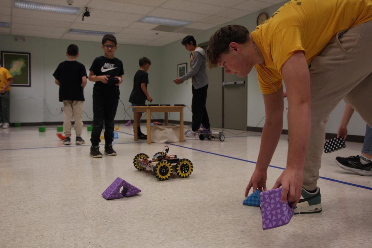 Brick by brick. Lee picks up the foam bricks that have fallen over after a student drives their robot through a stack they built prior. Each high school volunteer from the robotics team was paired up with a student to assist them while they drove the robots.