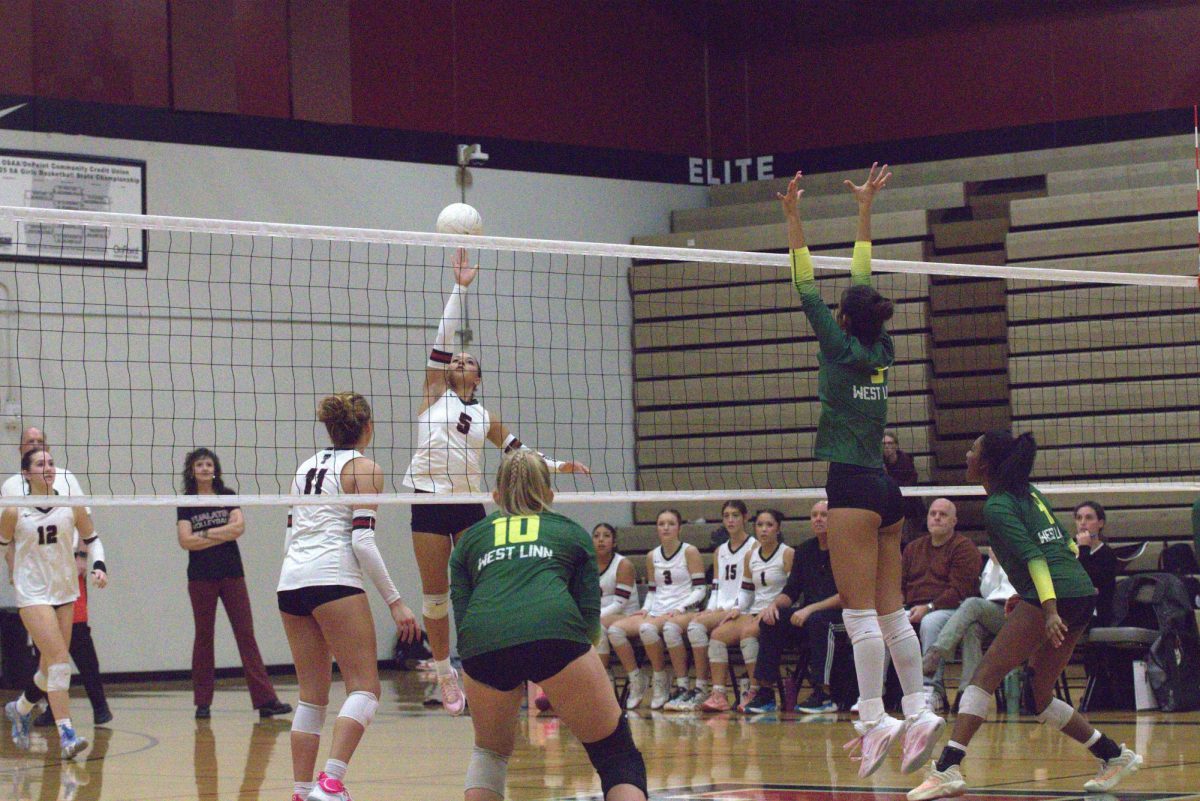 Battle at the net. A Tualatin player tips the ball over the net as Sophia Silva, junior, jumps up to block the ball. With only a few more points left to win, Silva defends the ball as Kennedy Toomer, senior, and Elise Bauer, freshman, get ready to protect the court.