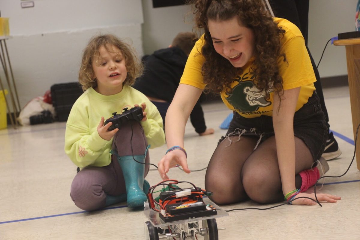 Helping hand. Ravenna Talaga, junior and outreach lead for the robotics team, helps replace the robot’s fallen costume. “I think Drive a Robot Day is a really good way to [think about the skill level] and expand that, because we're able to customize every single person's drive to every single kid,” Louis Cekay, junior, said. “We can have [a] kid where all you do is you just go in circles for 15 minutes because we don't want to push [their] boundaries too much.” 